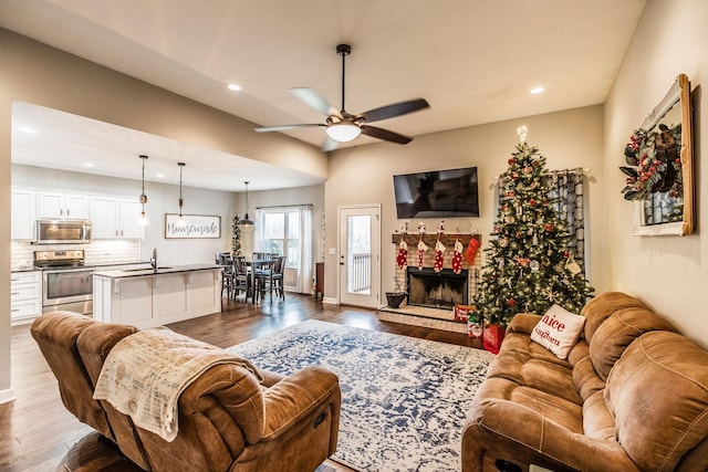 living room with dark hardwood / wood-style flooring, sink, a stone fireplace, and ceiling fan