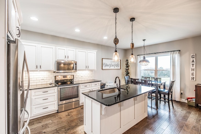 kitchen featuring appliances with stainless steel finishes, an island with sink, sink, white cabinets, and backsplash