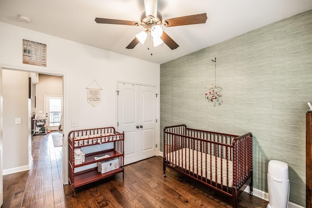 bedroom with dark hardwood / wood-style flooring, a nursery area, ceiling fan, and a closet