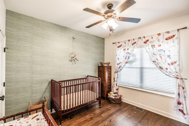 bedroom featuring multiple windows, a crib, dark hardwood / wood-style floors, and ceiling fan