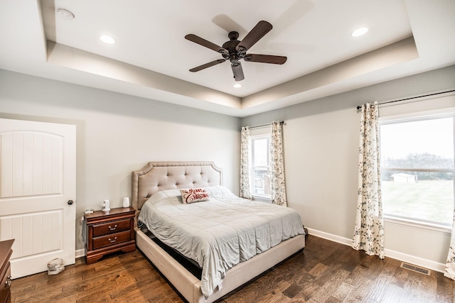 bedroom with multiple windows, dark hardwood / wood-style flooring, ceiling fan, and a tray ceiling