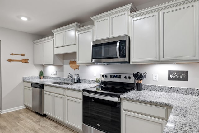 kitchen with sink, light stone countertops, light wood-type flooring, white cabinetry, and stainless steel appliances