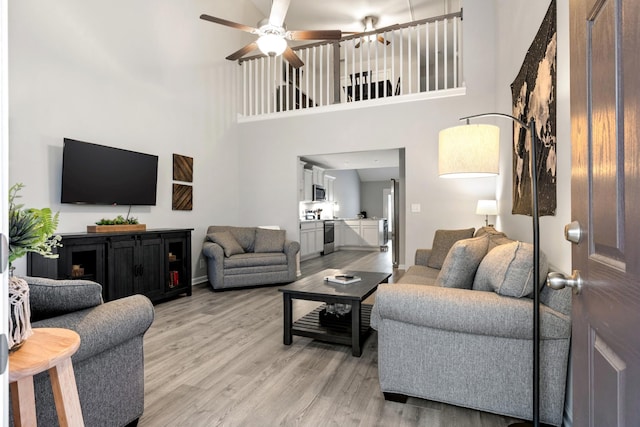 living room featuring ceiling fan, a towering ceiling, and light hardwood / wood-style floors