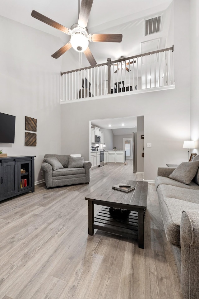 living room featuring a high ceiling, light wood-type flooring, and ceiling fan