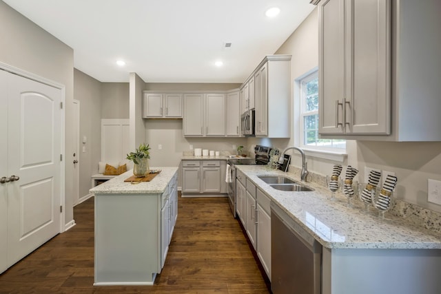 kitchen featuring light stone countertops, appliances with stainless steel finishes, a kitchen island, and dark wood-type flooring