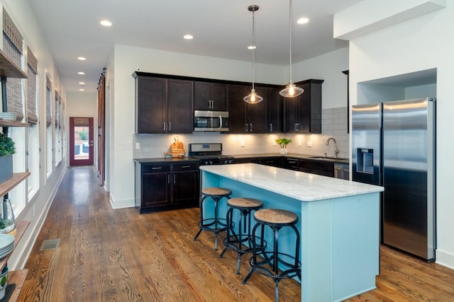 kitchen with hardwood / wood-style floors, sink, decorative light fixtures, a kitchen island, and stainless steel appliances