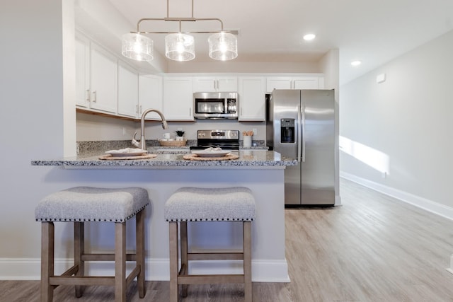 kitchen featuring kitchen peninsula, appliances with stainless steel finishes, light wood-type flooring, sink, and white cabinetry