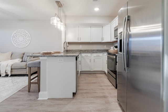 kitchen featuring decorative light fixtures, white cabinetry, stainless steel appliances, and light hardwood / wood-style flooring