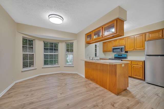 kitchen with kitchen peninsula, a textured ceiling, light wood-type flooring, and stainless steel appliances