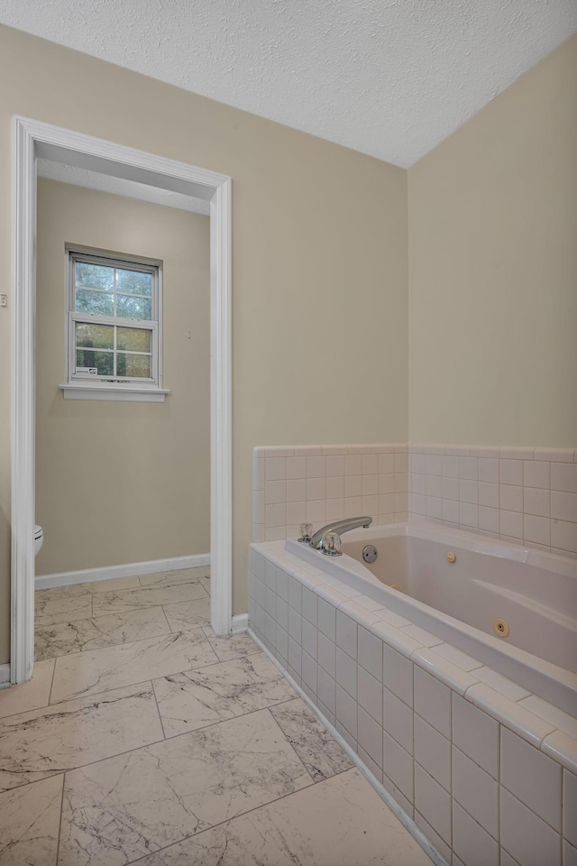 bathroom featuring a textured ceiling, a relaxing tiled tub, and toilet