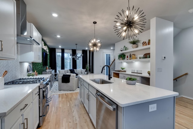 kitchen featuring decorative light fixtures, wall chimney exhaust hood, an island with sink, appliances with stainless steel finishes, and a notable chandelier