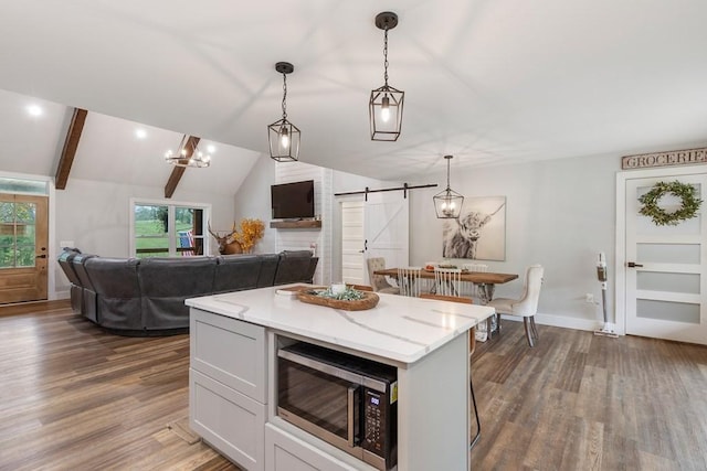 kitchen featuring pendant lighting, lofted ceiling with beams, a barn door, light stone counters, and dark hardwood / wood-style flooring