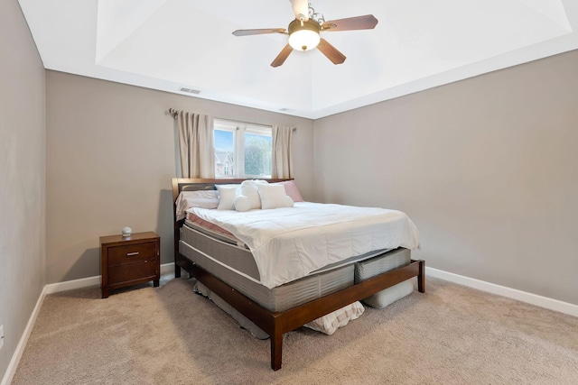 bedroom with a raised ceiling, ceiling fan, and light colored carpet