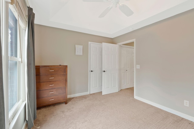 unfurnished bedroom featuring light colored carpet, ceiling fan, and a tray ceiling