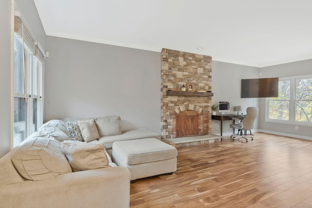 living room featuring a stone fireplace, crown molding, and light hardwood / wood-style floors