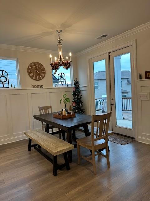 dining space with a notable chandelier, ornamental molding, wood finished floors, and a decorative wall