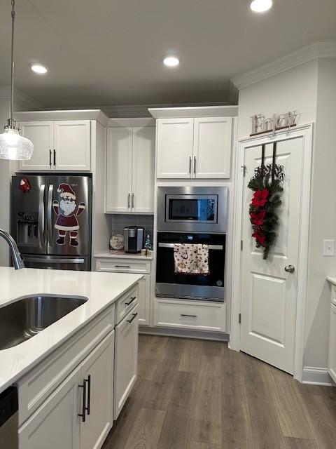 kitchen featuring stainless steel appliances, dark wood-type flooring, ornamental molding, white cabinetry, and a sink