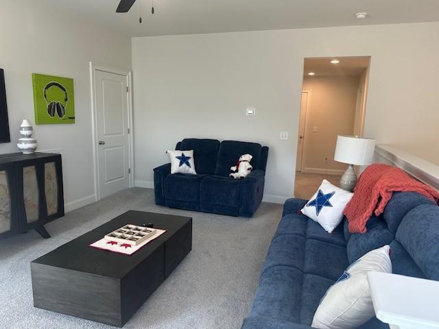 living area with a ceiling fan, baseboards, and carpet flooring