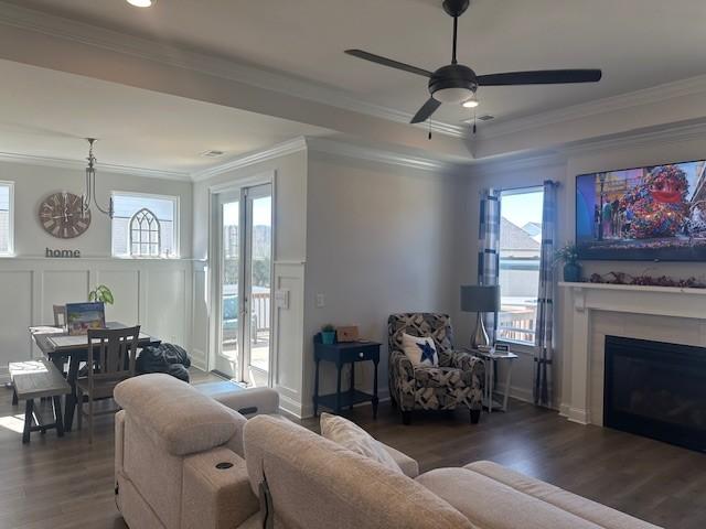 living area with a wainscoted wall, a decorative wall, ornamental molding, a glass covered fireplace, and wood finished floors