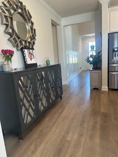 hallway featuring a wainscoted wall, ornamental molding, a decorative wall, and wood finished floors