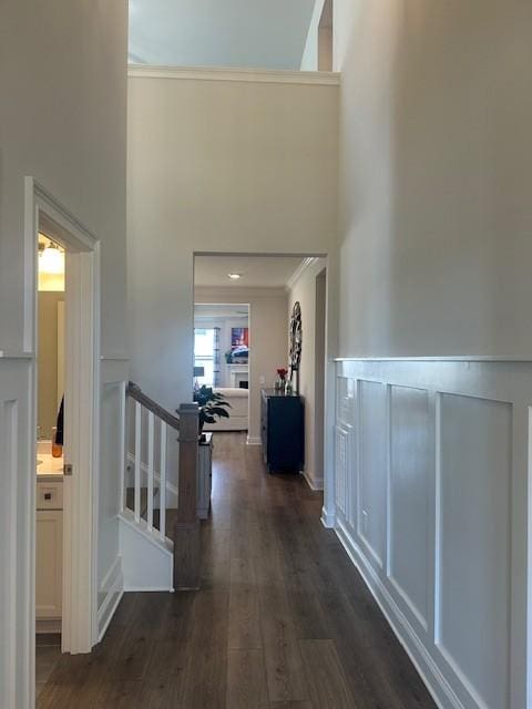 corridor featuring a towering ceiling, crown molding, wood finished floors, and an upstairs landing