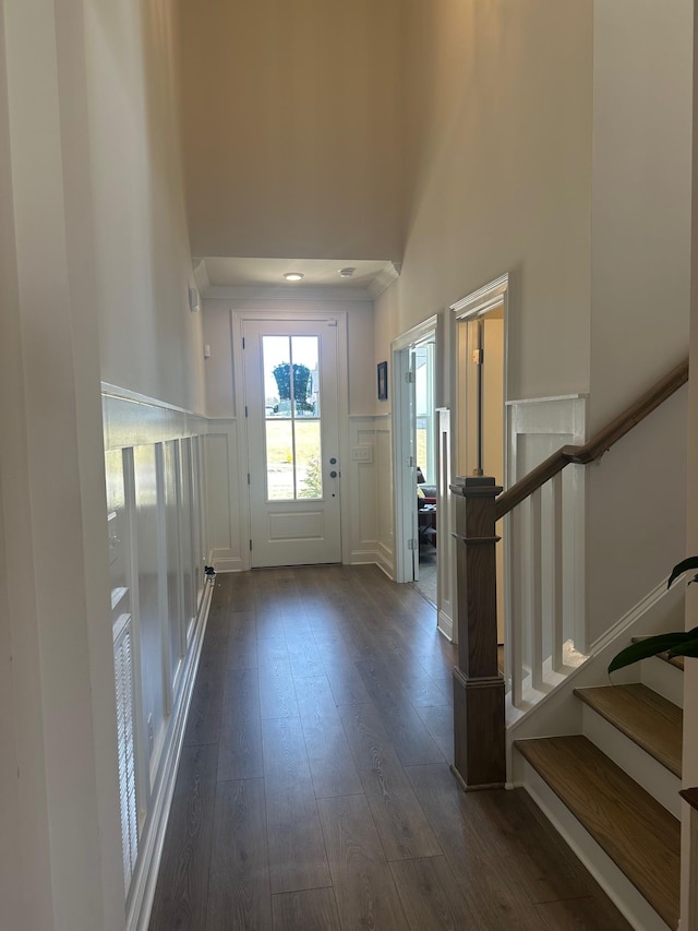 doorway to outside with a decorative wall, a wainscoted wall, a high ceiling, stairway, and dark wood finished floors