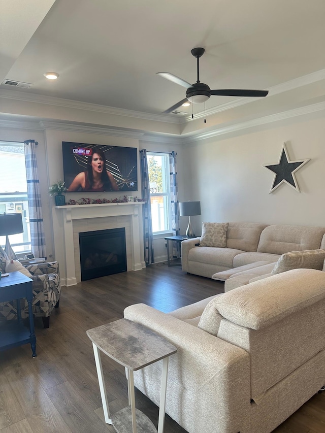 living room featuring visible vents, a ceiling fan, a glass covered fireplace, ornamental molding, and wood finished floors