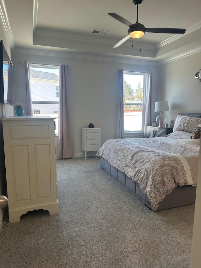 carpeted bedroom with ceiling fan, a raised ceiling, visible vents, and crown molding