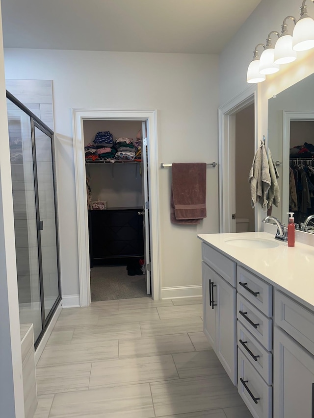 bathroom with a stall shower, vanity, baseboards, and a spacious closet