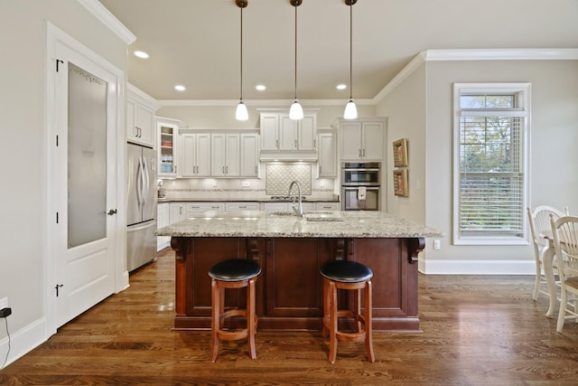 kitchen featuring pendant lighting, dark wood-type flooring, a center island with sink, appliances with stainless steel finishes, and light stone counters