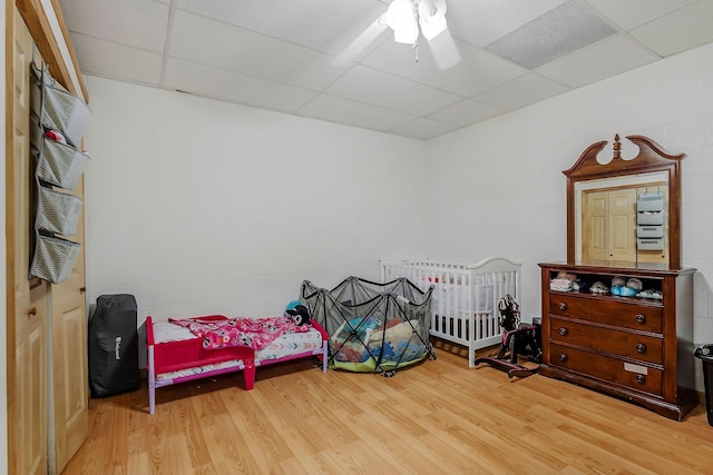 bedroom featuring ceiling fan, a drop ceiling, and wood-type flooring