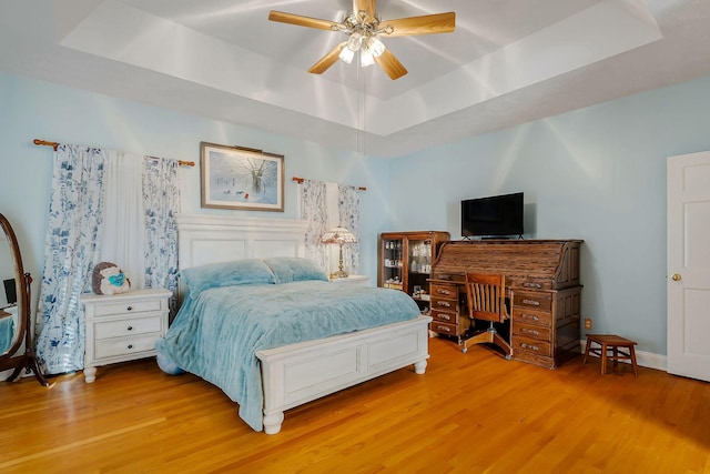 bedroom featuring light wood-type flooring, a raised ceiling, and ceiling fan