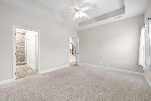 spare room featuring light carpet, a tray ceiling, and ceiling fan