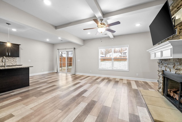 unfurnished living room with sink, ceiling fan, beam ceiling, a fireplace, and light wood-type flooring