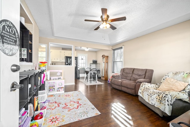 living room with dark hardwood / wood-style floors, ceiling fan, a textured ceiling, and a tray ceiling