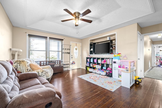 living room featuring a textured ceiling, ceiling fan, dark wood-type flooring, and a tray ceiling