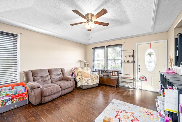 living room with a textured ceiling, ceiling fan, a raised ceiling, and dark wood-type flooring