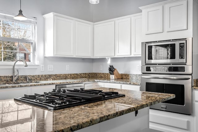 kitchen with pendant lighting, dark stone counters, sink, white cabinetry, and stainless steel appliances