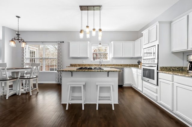 kitchen with white cabinetry, stainless steel appliances, dark hardwood / wood-style floors, dark stone countertops, and decorative light fixtures