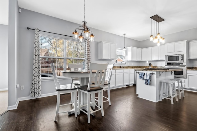 kitchen featuring hanging light fixtures, stainless steel appliances, a kitchen island, a breakfast bar area, and white cabinets