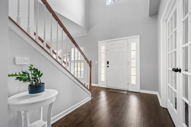 foyer entrance with dark wood-type flooring and high vaulted ceiling