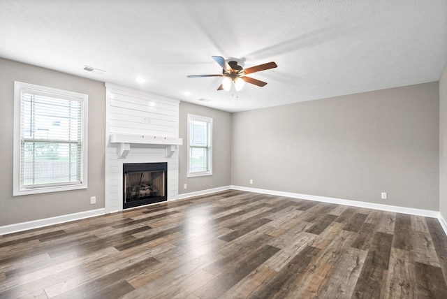 unfurnished living room featuring a fireplace, a textured ceiling, dark hardwood / wood-style floors, and plenty of natural light