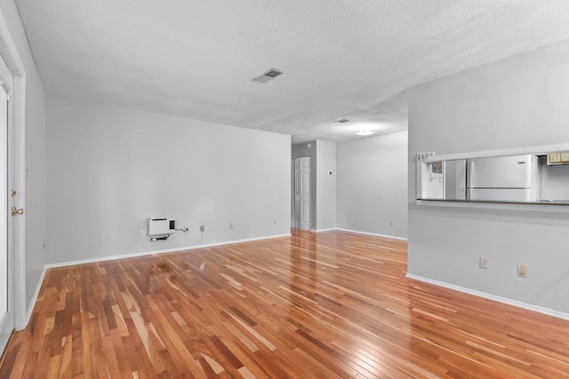 empty room featuring a textured ceiling, light wood-type flooring, and heating unit