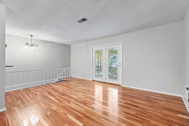 empty room with wood-type flooring, a textured ceiling, and an inviting chandelier