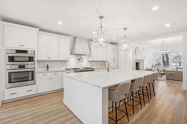 kitchen with white cabinets, a large island, sink, and premium range hood