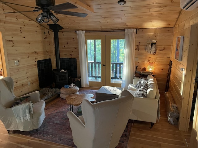 living room with a wood stove, french doors, a wall unit AC, hardwood / wood-style floors, and vaulted ceiling