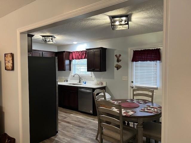 kitchen with dishwasher, black refrigerator, sink, light wood-type flooring, and dark brown cabinets