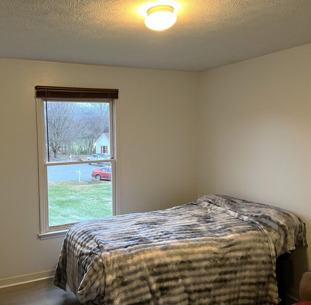 bedroom with a textured ceiling, dark hardwood / wood-style floors, and multiple windows