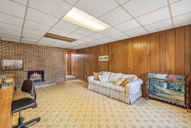 living room featuring a fireplace, a drop ceiling, wooden walls, and brick wall