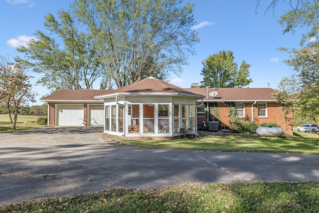 view of front facade with a sunroom, a front lawn, central AC unit, and a garage